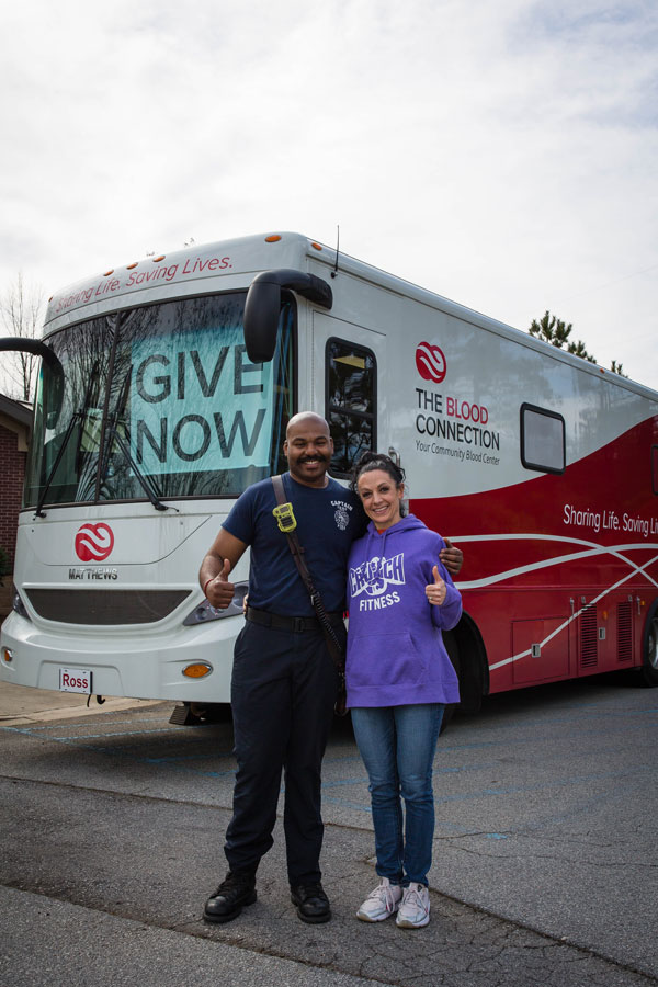 Firefighter smiling with woman in front of The Blood Connection mobile Blood Center. 
